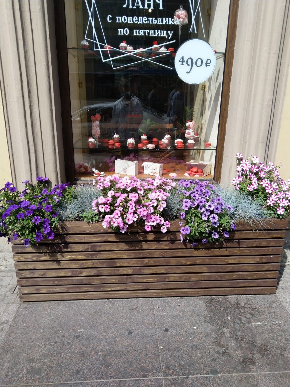 Уличная композиция из разноцветных петуний и зелени в стильном кашпо, подчёркивающая уют витрины.